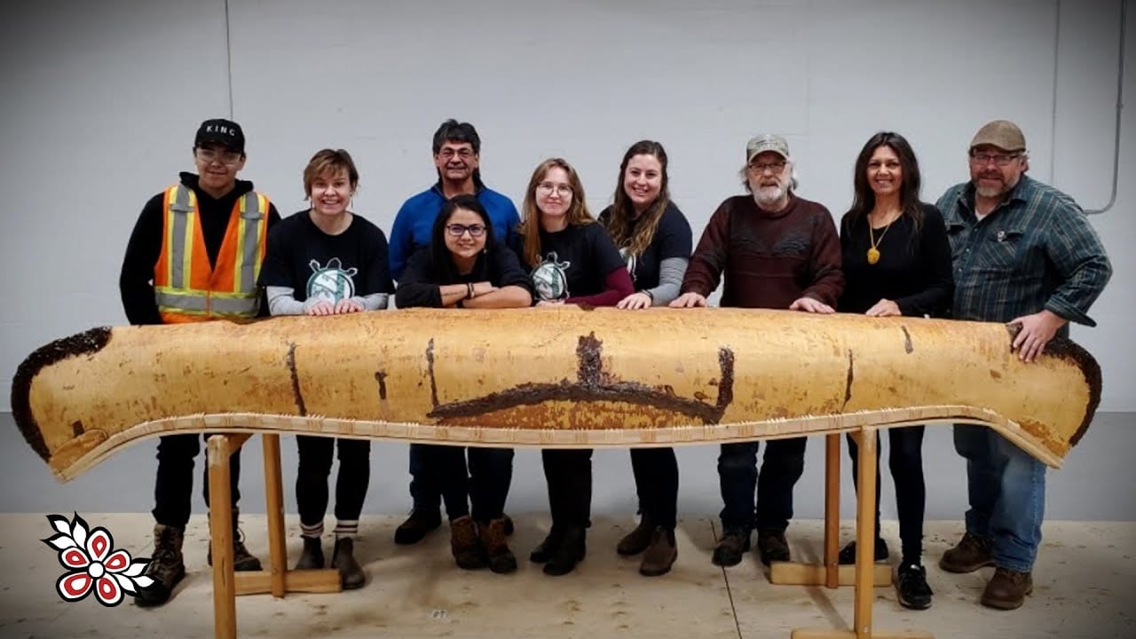 a group of people standing behind a wooden canoe on display