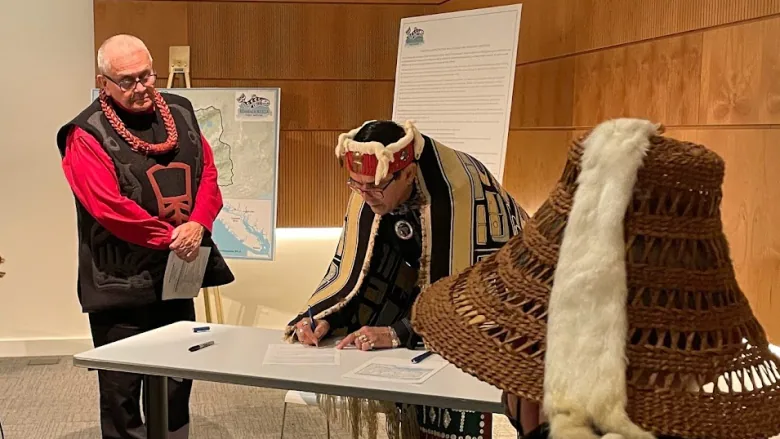 Mamalilikulla Chief Councillor John Powell is seen standing and signing a paper at a table.